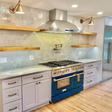 Modern kitchen with a blue stove, ProlineRangeHoods.com's ProSW.42 wall-mounted 1800 CFM dual motor range hood, marble countertop, and wooden shelves on a tiled backsplash.